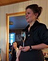 Kvinne med champagneglass taler til gjester i en stue