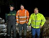 Tre personer i arbeids- og refleksklær står ute i mørket på en våt vei.