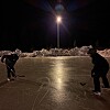 To personer spiller ishockey på en opplyst utendørs isbane om natten.
