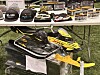 Utstillingsbord med Ski-Doo luer, modeller og en liten gul og svart snøscooter.