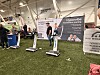 Messehall med stands, treningsmaskiner og besøkende på kunstgress.