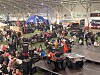 Stor innendørs messe med snøscootere, firehjulinger og mange besøkende ved bord og utstillere.