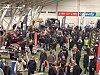 Mange mennesker går mellom stands med snøscootere og utstyr inne i en stor messehall.