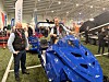 To personer ved en blå beltebil på en innendørs snøscooter- og fritidsmesse.