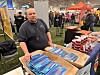 Mann bak stand med pakker med røyket fisk og bokser med mat på innendørs messe.