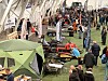 Innendørs messe med mange besøkende, snøscootere og utstyr utstilt langs en grønn kunstgressbane.