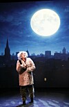Skuespiller i pelskostyme på scene foran bysilhuett og stor fullmåne.