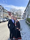 Et par står sammen i en solfylt gate med rekkehus, parkerte biler og nakne trær i bakgrunnen.