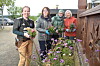 Fire personer står ved et blomsterbed og holder buketter utenfor en bygning.
