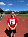 Person i rød T-skjorte med startnummer 77 står på en rød friidrettsbane i solskinn.
