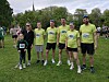 En gruppe løpere i gule T-skjorter står samlet på gresset i en park før et mosjonsløp.